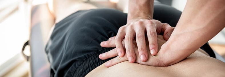 Therapist giving lower back sports massage to athlete male patient in clinic